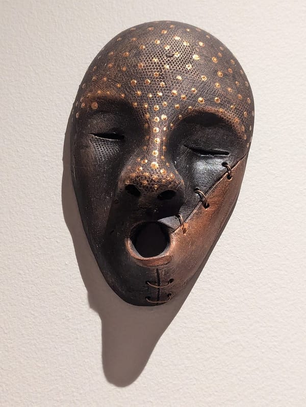 A native mask in leather and metal of unknown origin, the eyes are horizontal slits, and the nose and forehead are dotted wit